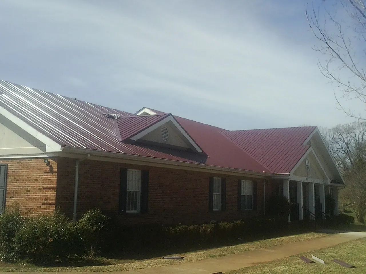 Red metal roof with gabled entries on a long brick building, from a Hail Damage Roof Repair job in Verdugo City