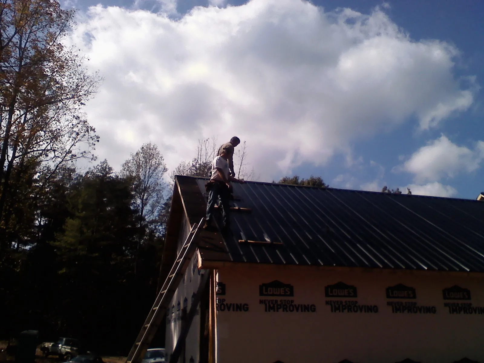 Roofer fastening dark metal panels high against a cloudy sky, from a Roof Inspection job in Verdugo City