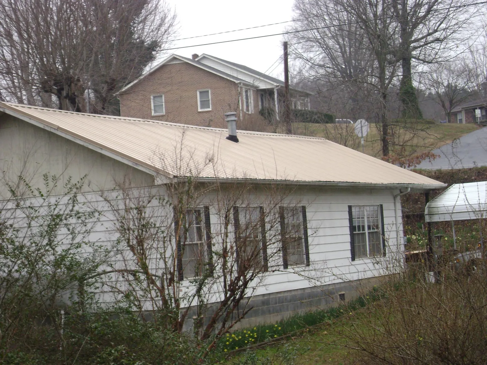 Tan metal roof on a white sided house set into a hillside — Commercial Roofing by Roofing Brothers in Verdugo City